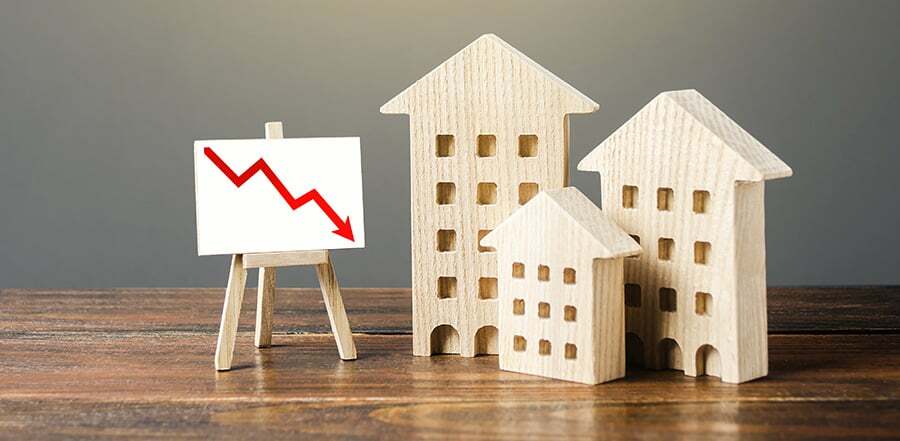 Wooden houses residential buildings and an easel with a red down arrow. Fall of real estate market. Value cost decrease. Bad liquidity attractiveness. Cheap rent. Reduced demand, recession. Low sales